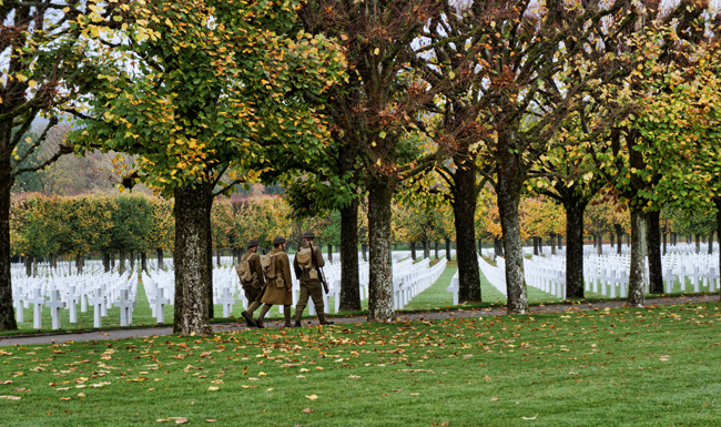 Photograph of soldiers in World War I battle gear walking past the headstones at Meuse-Argonne American Cemetery on Veterans Day 2015.